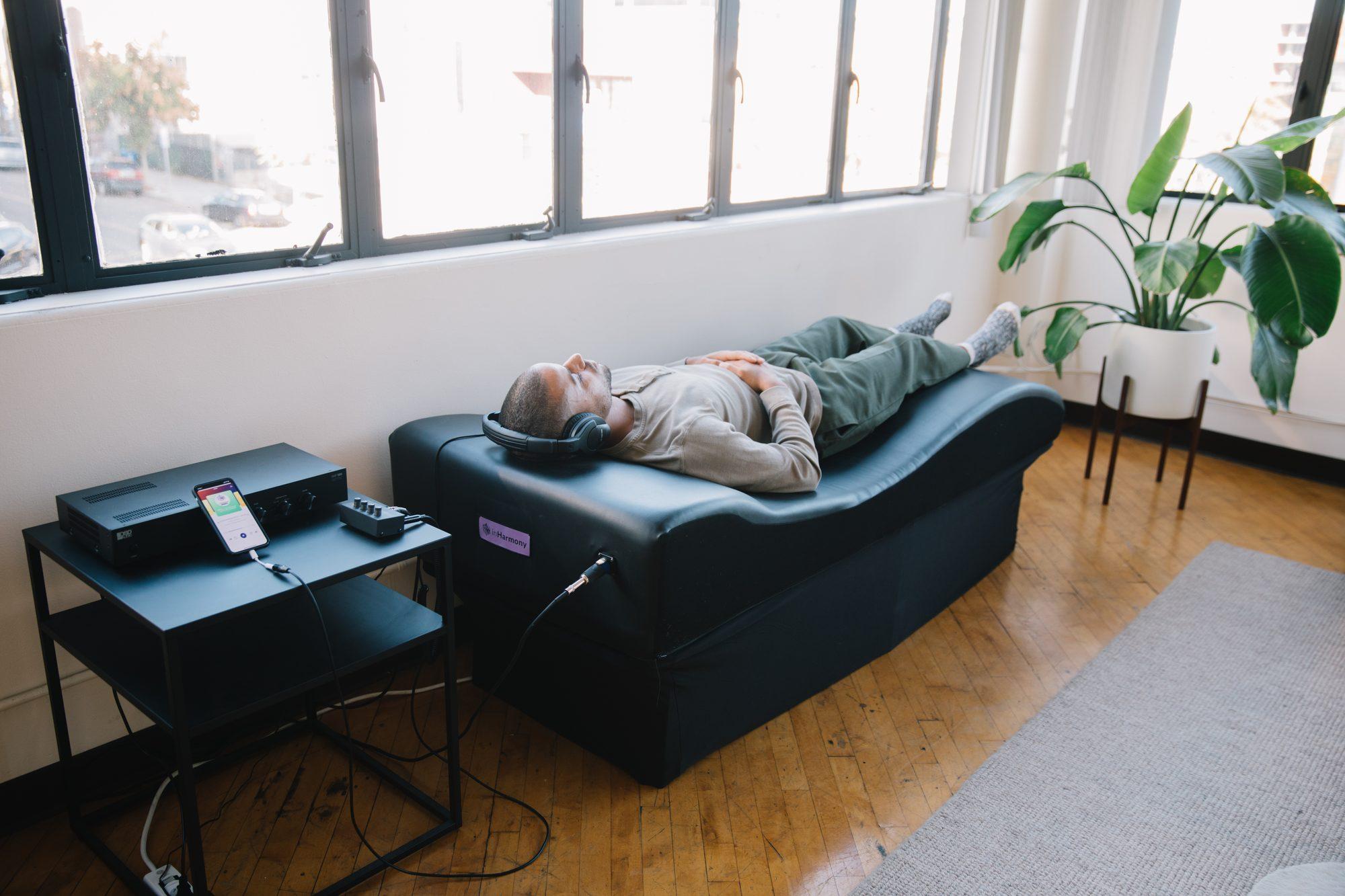 A person lying fully clothed on the vibroacoustic table with headphones on, in a bright room