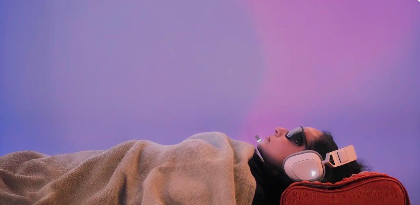 A person under a blanket wearing SoundSelf light glasses and headphones