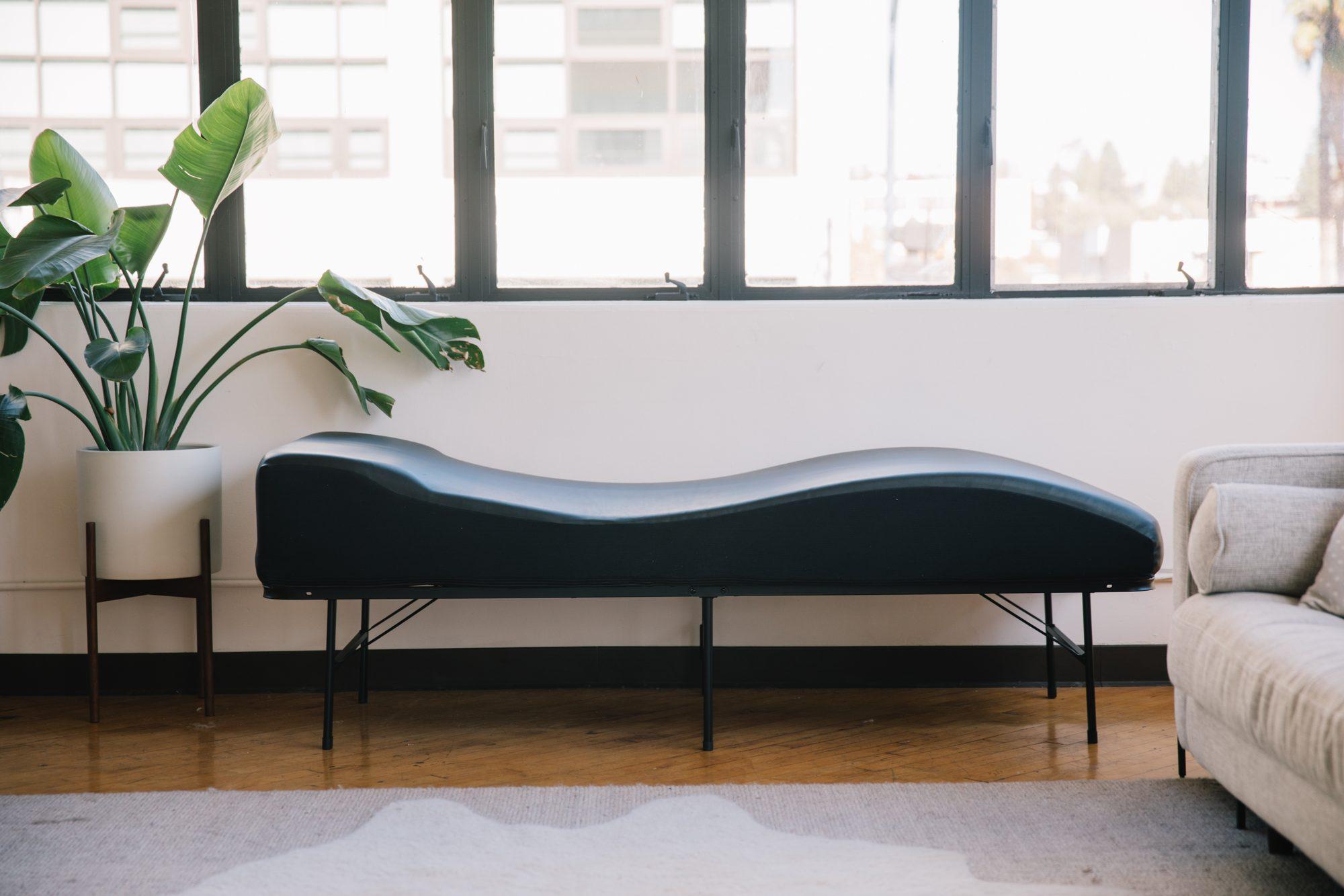 The vibroacoustic table in a bright room by a window, with a plant beside it